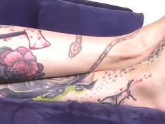 Barefoot blue eyed tattoed girl gives herself a foot massage