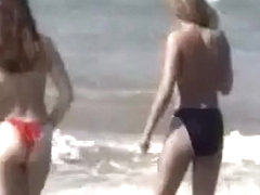 Due teen bionde camminano sulla sabbia in topless